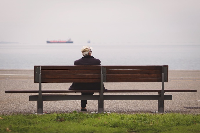 Hombre sentado en un banco en la playa mirando al mar